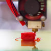 A 3D printer creates a small red part that will be used in the manufacturing of farming equipment.