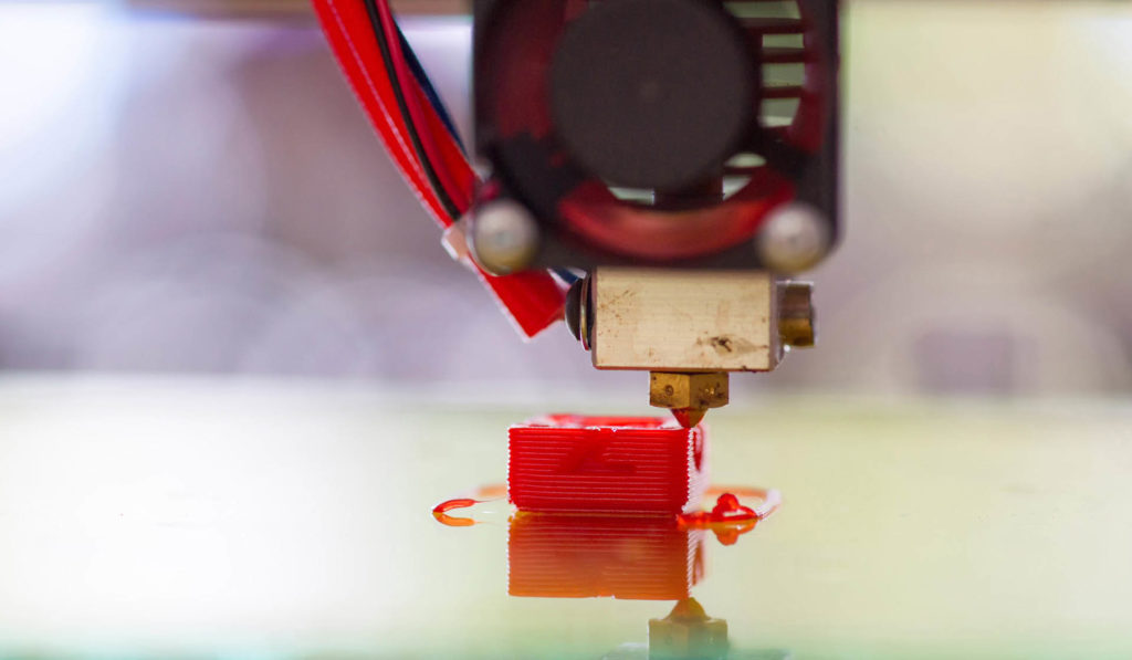 A 3D printer creates a small red part that will be used in the manufacturing of farming equipment.